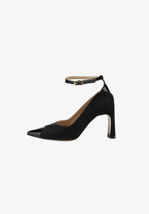 Escarpin noir en suède avec un bout pointu noir brillant, une bride à la cheville avec une boucle dorée et un talon transparent. Texture lisse dans l'ensemble.