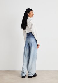 Ανοιχτό μπλε φαρδιές τζιν παντελόνες με ψηλή μέση και ανοιχτόχρωμη υφή, συνδυασμένες με ένα άσπρο πουκάμισο με κουμπιά. Απαλή υφή και χαλαρή εφαρμογή.