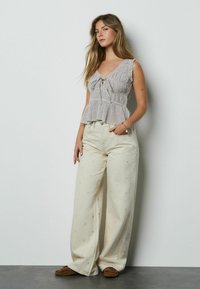 Ruuduline peplumi-stiilis pluus ees lipsuga, koos laiade beežide pükstega, millel on südamekirju muster, täiendatud pruunide libisemiskingadega.