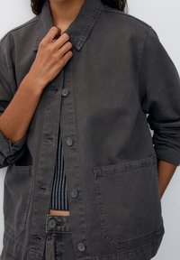 Giacca utilitaria grigio scuro con colletto, chiusura centrale a bottoni e due tasche frontali. Realizzata in un tessuto testurizzato con una vestibilità comoda.