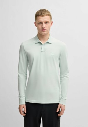 Langarm poloshirt in licht muntgroen, gemaakt van zachte stof. Bevat een kraag, een drieknoopssluiting en een klein logopatch op de borst.