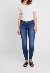 Smal blå jeans med en klassisk design med fem fickor, parat med en vit t-shirt med kort ärm och svarta nitar sandaler.