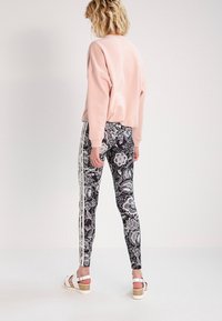 Vaaleanpunainen lyhyt huppari pitkillä hihoilla, yhdistettynä mustiin legginsseihin, joissa on valkoinen kukkakuosi ja kolme valkoista sivuraitaa.