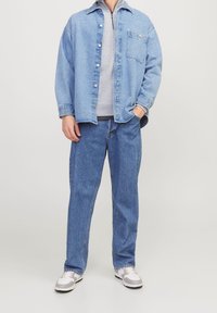 Světlá modrá džínová košile s knoflíky, pod ní šedá fleecová mikina, modré džíny a šedé tenisky s bílými detaily.