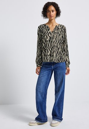 Blusa de manga larga con estampado animal en beige y negro, con escote en V y corte relajado, combinada con jeans de pierna ancha en azul y zapatillas casuales.