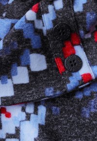 Tessuto grigio con un motivo pixelato in rosso, blu e azzurro. Sono visibili due bottoni neri con la scritta "CECIL" in rilievo.