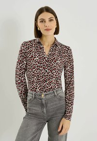 Camisa abotonada con base blanca, estampado de leopardo en rojo y negro, mangas largas y cuello clásico, combinada con jeans grises de talle alto.