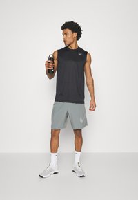 Sort ærmeløs atletisk top, grå shorts med logo, sort sport vandflaske, hvide strømper og grå sneakers med accenter.