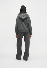 Γκρι φούτερ με κουκούλα και άνετη εφαρμογή, συνδυασμένο με ταιριαστό γκρι παντελόνι φόρμας. Μαλακή υφή, ορατές ραφές στις άκρες και απλός σχεδιασμός.