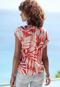 Blusa a maniche corte, rossa e bianca con motivo floreale, dal taglio rilassato, realizzata in tessuto leggero, con una cucitura sul retro e una superficie liscia.
