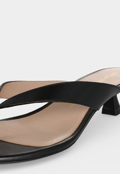 Mule sandale noire à bout ouvert avec deux brides croisées et un petit talon bloc, avec une semelle intérieure beige et une finition lisse.