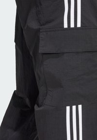 Svarta cargobyxor i tyg med texturerad yta, stor sidoficka och tre vita vertikala ränder längs sidan.