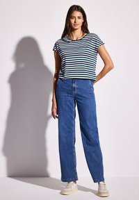 Camiseta a rayas con líneas verdes, blancas y rosas, combinada con jeans de pierna ancha de talle alto en azul y zapatillas de color claro.