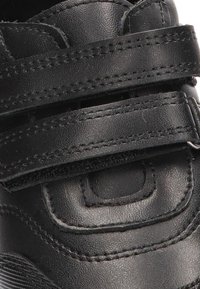 Zapatilla deportiva negra con parte superior de cuero texturizado. Cuenta con dos correas ajustables de Velcro y soporte acolchado en el tobillo para mayor comodidad.