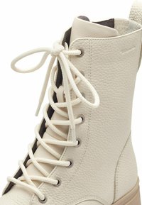 Stivale alto in pelle bianca con superficie rotonda e texturizzata, occhielli in metallo e suola spessa in gomma beige. I lacci sono leggermente allentati.
