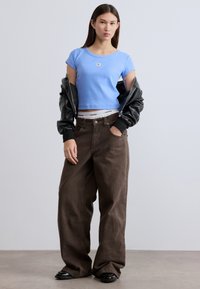 Φωτεινό γαλάζιο κοντό μπλουζάκι με μικρό λογότυπο, συνδυασμένο με χαλαρά καφέ σκούρα παντελόνια και μαύρο δερμάτινο μπουφάν. Μαύρα παπούτσια.