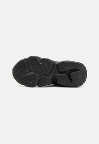 Suela de zapatilla negra con un diseño texturizado que presenta surcos y patrones para tracción. El material parece caucho con formas geométricas.