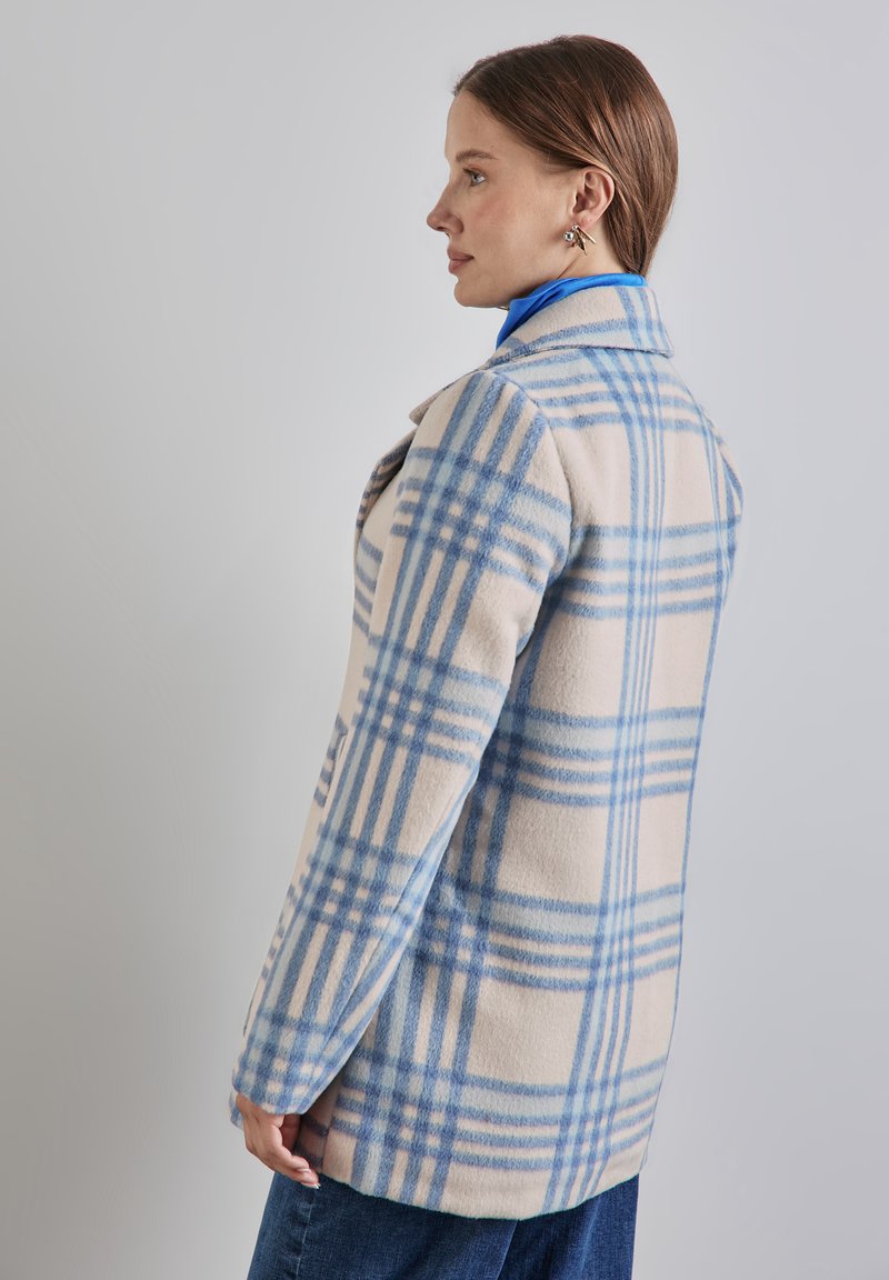 Kevyt ruutukuosi takki vaaleassa sävyssä, jossa on sinisiä tarkistuksia. Takissa on klassinen kaulus ja sivutaskut, ja se on valmistettu pehmeästä, teksturoidusta villamaisesta kankaasta.