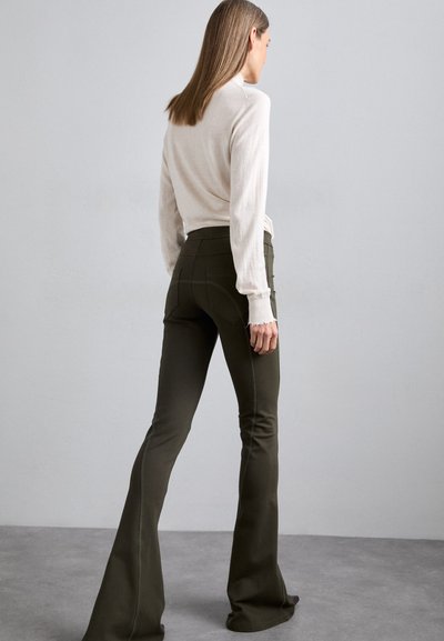 Olijfgroene flared broek van textuurstof, met een hoge taille en gedetailleerde stiksels, gecombineerd met een lichtbeige lange mouwtop.