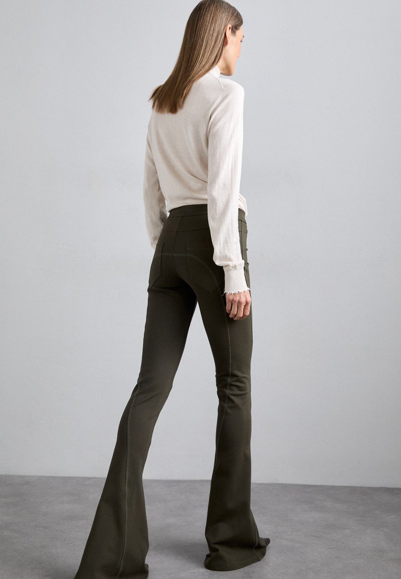 Olive green flared pants made of textured fabric, feature a high waist and detailed stitching, paired with a light beige long-sleeve top.
