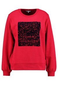 Rood sweatshirt met een zwart vierkant grafisch ontwerp met een bloemmotief en "TOMMY HILFIGER" tekst. Geribbelde manchetten en neklijn. Zacht materiaal.