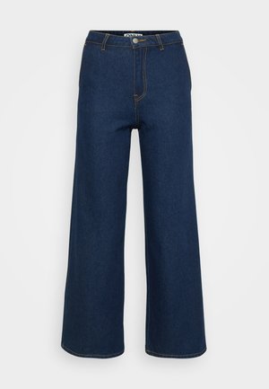 Pantalons en denim à jambe large de couleur bleu foncé avec des surpiqûres jaunes en contraste, taille haute et fermeture à bouton. Texture lisse et design classique.