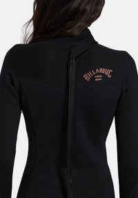 Schwarzer Neoprenanzug mit tailliertem Design, ausgestattet mit einem Reißverschluss auf dem Rücken und einem roten "Billabong"-Logo auf dem oberen Rücken. Glatte Oberfläche.