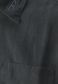 Dark gray linen shirt featuring a fold-down collar, a chest pocket, and an embroidered logo on the collar. Soft texture with a slightly wrinkled appearance.