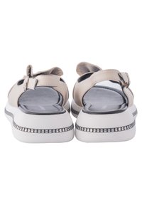 Sandales en cuir beige avec sangle ajustable, semelle intérieure grise rembourrée et semelle blanche dotée d'un accent décoratif noir et argent.