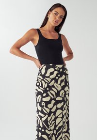 Musta ribattu tank top yhdistettynä lattiaan ulottuvaan hameeseen, jossa on abstrakti kerma- ja mustakuosis, mikä korostaa istuvaa siluettia ja tekstuurin kontrastia.