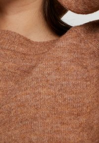 Pull en tricot marron avec un col côtelé, présentant un tissu doux et texturé ainsi que des variations subtiles de couleur sur l'ensemble.