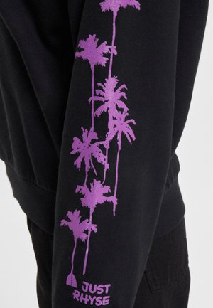 Juodas sportinis megztinis su vertikaliu purpurinių palmės medžių dizainu ant vienos rankovės ir tekstu "JUST RHYSE" šalia rankogaliaus, minkšta tekstūra.