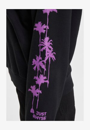 Sudadera negra con un diseño vertical de palmeras moradas en una manga y el texto "JUST RHYSE" cerca del puño, con textura suave.
