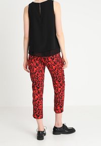 Svart ärmlös blus med ett nyckelhål baktill, ihop med röda byxor med ett svart djurtrycksmönster och svarta snörskor.