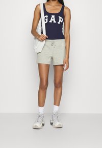 Canottiera navy con logo bianco "GAP", pantaloni grigi con coulisse e dettagli del logo, calzini bianchi alla caviglia e scarpe sportive grigie.