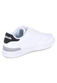 Zapatilla deportiva blanca con parte superior sintética lisa, detalles texturizados en gris y negro en el talón, y suela de goma blanca.