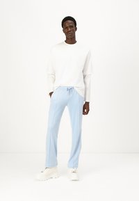 Pantaloni della tuta blu chiaro con vita regolabile, cuciture laterali a contrasto e vestibilità rilassata, abbinati a una maglietta bianca a maniche lunghe e sneaker bianche.
