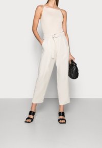 Body beige a costine con spalline sottili, abbinato a pantaloni chiari color crema a vita alta con cintura. Borsa nera e sandali con tacco.