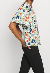 Blommig peplumtop i ljusblått, med röda, orange och marinblå blommor. Kortsleeves, insamlad midja, lättviktig tyg. I kombination med svarta byxor.