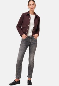 Veste bordeaux avec poches avant et boutons en argent, associée à un jean gris et des mocassins noirs. Design simple, coupe ajustée.
