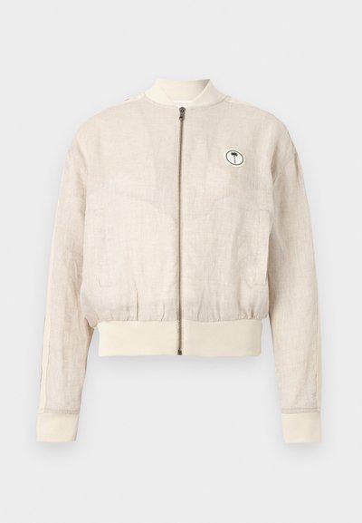 Μπεζ μπουφάν bomber από λινό με μπροστινό φερμουάρ, ριμπ μανσέτες και τελείωμα, πλαϊνές τσέπες και μικρό στρογγυλό πατς με φοινικόδεντρο στο στήθος.
