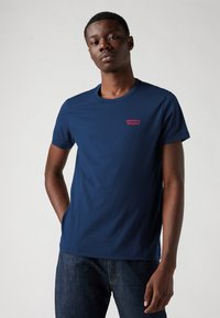 Marineblauwe katoenen t-shirt met een ronde hals en korte mouwen; heeft een klein rood Levi's logo op de linkerkant van de borst.