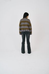 Bóbitott fazonú pulóver zöld és szürke csíkokkal, flared fekete farmernadrággal párosítva. A textúrája puhanak és melegnek tűnik.