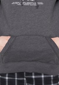 Grå sweatshirt med känguruficka, snörning och vit text som listar olika städer i Kalifornien. Ribbad manschetter och nederkant.