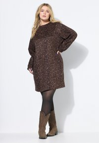 Bruine jurk met luipaardprint, lange mouwen, een ronde hals en een comfortabele pasvorm. Een paar tan cowboylaarzen met decoratieve accenten.