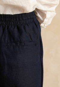 Tumesinised lahtised püksid, millel on elastne vöökoht ja üks tagatasku lamedate õmblustega, valmistatud pehmest, tekstuuriga kangast.