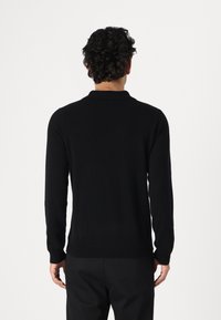 Maglione polo a maniche lunghe nero, realizzato in tessuto morbido, con colletto e orlo dritto, visto da dietro.