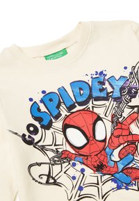 Krémová bavlněná košile s dlouhým rukávem, která je zdobena grafikou Spider-Mana s modrými a černými akcenty a textem "Go Spidey" v tučných modrých písmenech.