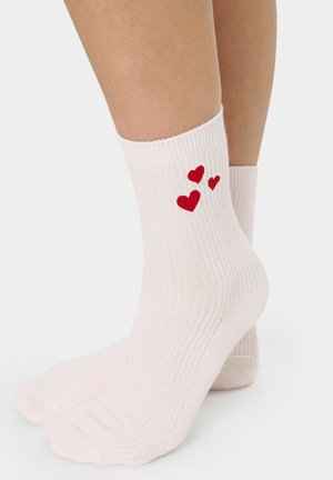 Calze alla caviglia rosa a coste con tre cuori rosse ricamate sul lato esterno. Materiale in misto cotone, texture morbida e traspirante.