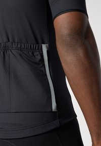 T-shirt de sport noir à manches courtes avec un tissu texturé, une ceinture élastique et une poche latérale avec un accent gris.